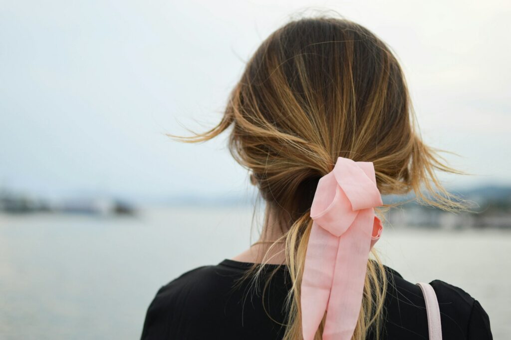 focus photography of woman with pink hair bow facing on body of water